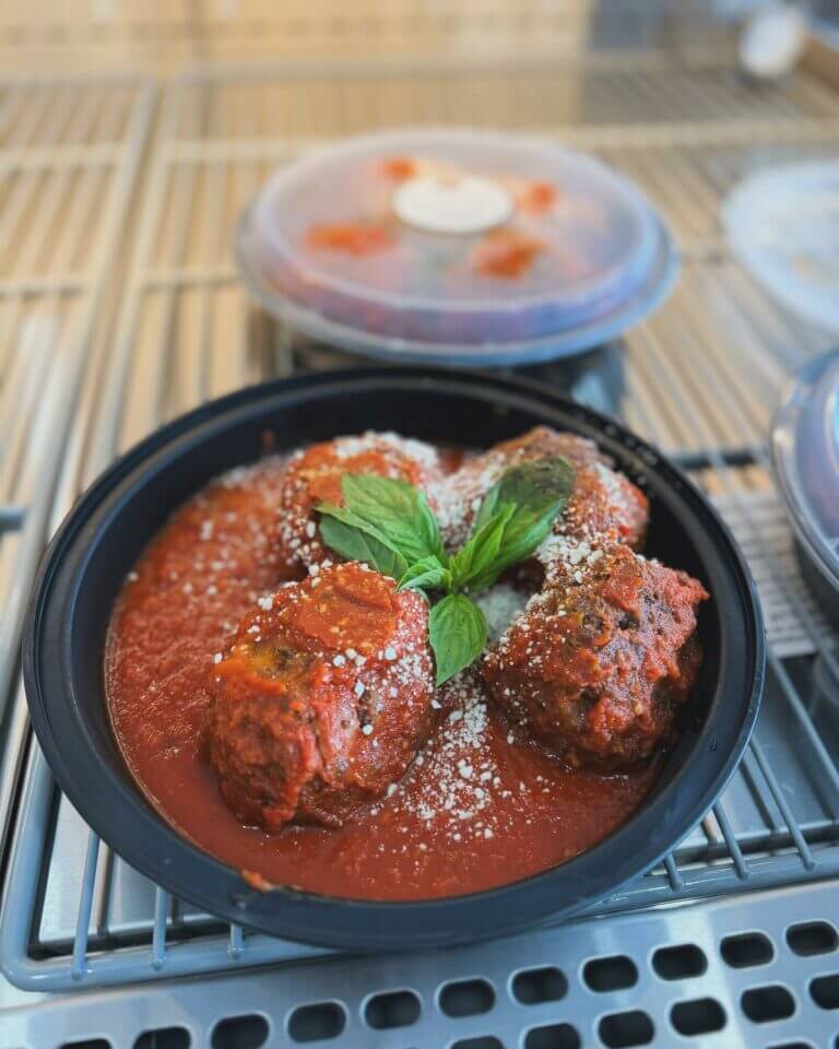 Black bowl with Italian meatballs in rich tomato sauce, garnished with fresh basil and Parmesan, on a cooling rack.