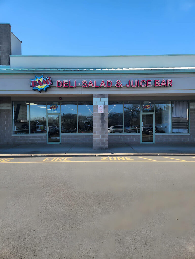 Exterior of BAM! Deli, Salad & Juice Bar with clear blue sky and parking area, inviting healthy dining options.