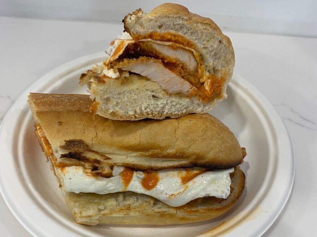 Grilled chicken sandwich with mozzarella and marinara on a crusty roll, served on a white plate, delicious lunch option.