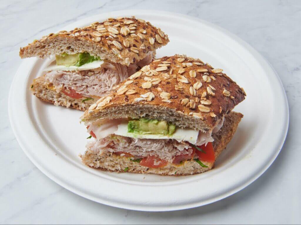 Whole grain turkey sandwich with avocado, tomato, and lettuce on a plate. Healthy lunch option, fiber-rich bread, fresh ingredients.