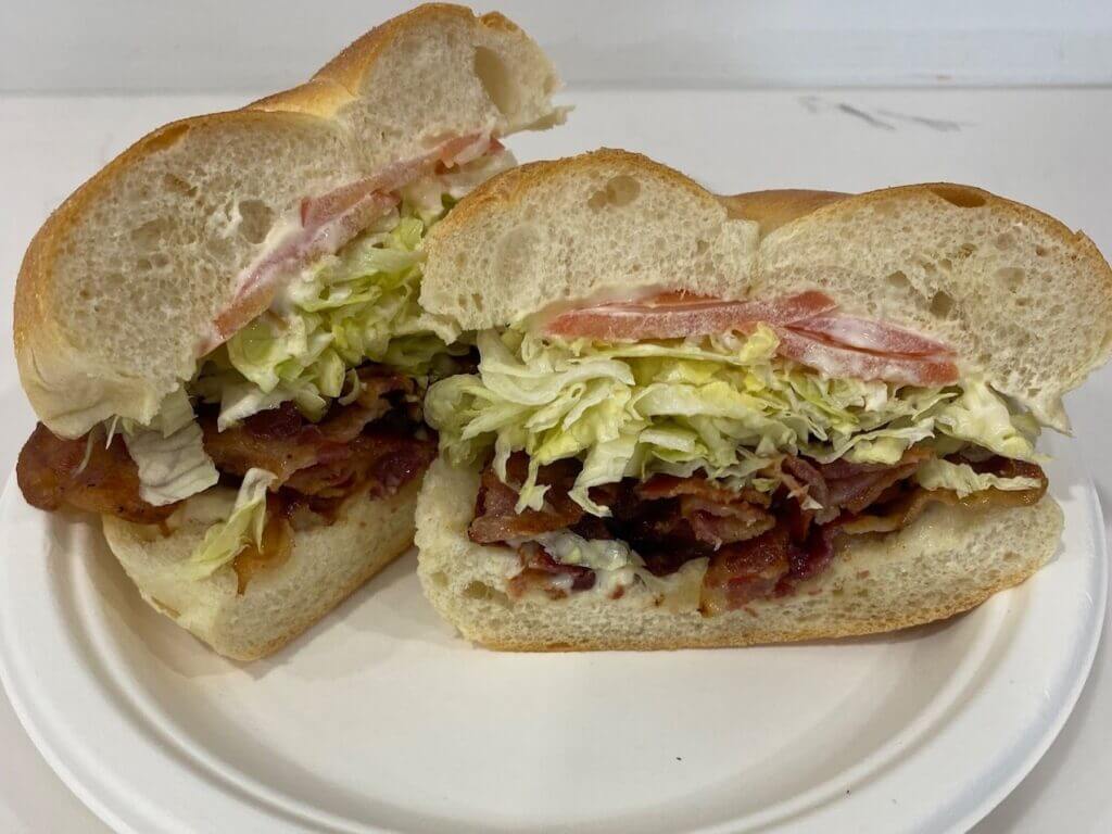 BLT sandwich with crispy bacon, fresh lettuce, tomato on a sliced roll, served on a white plate. Perfect for lunch or brunch.
