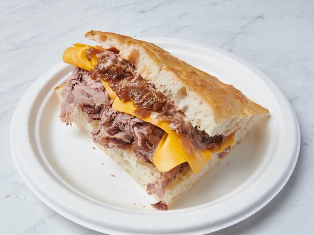 Roast beef sandwich with cheddar cheese and caramelized onions on a white plate.