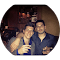 Two friends enjoying drinks at a dimly lit bar, smiling and embracing, creating a warm, festive atmosphere.